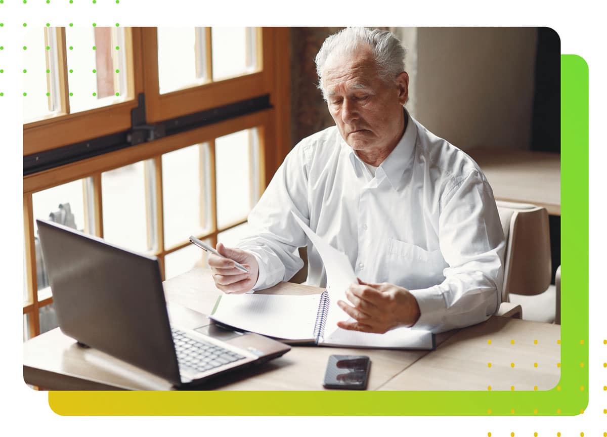 A man in front of a laptop holding a pen and a paper