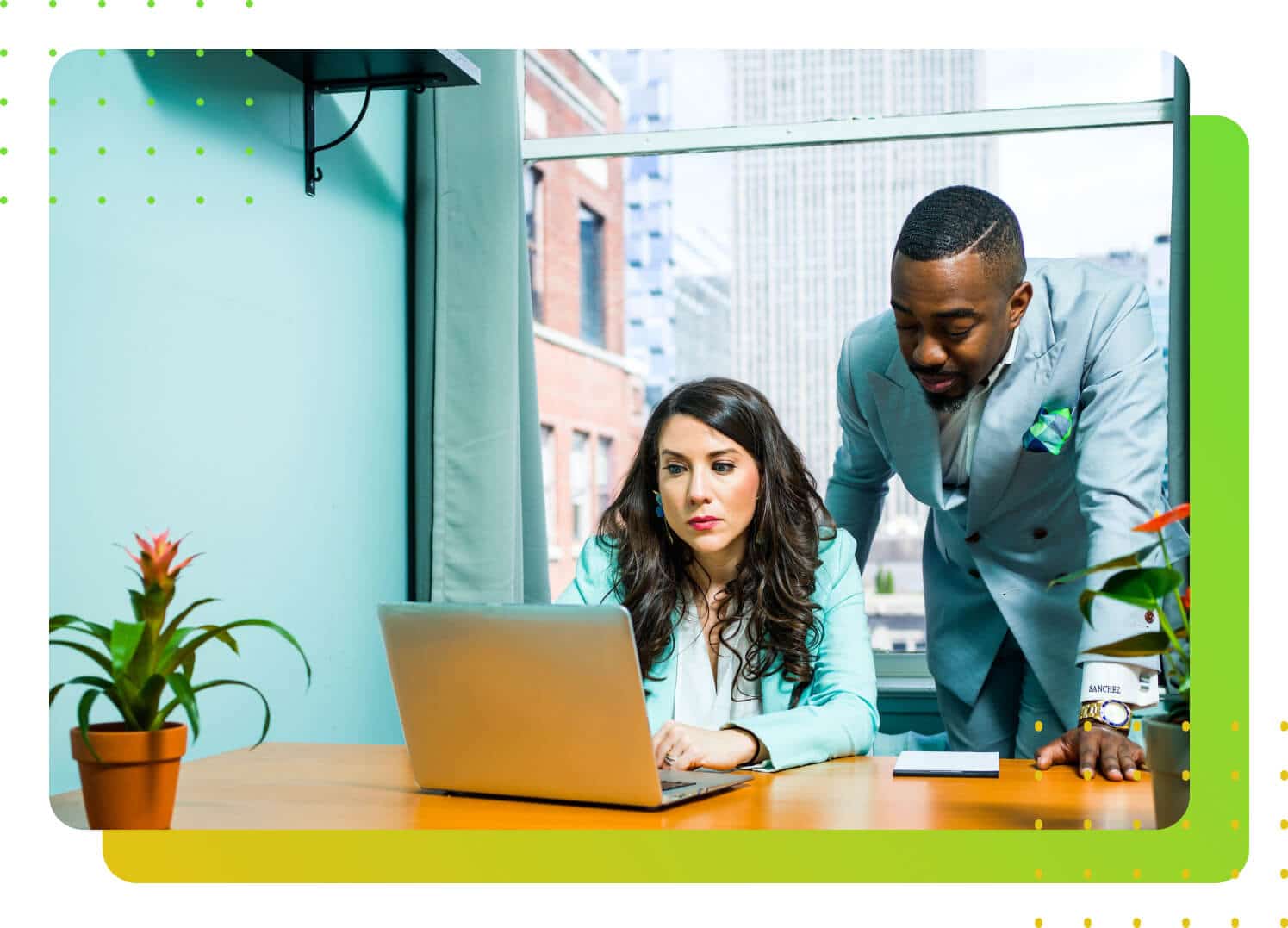 A man in suit standing over a lady in suit while they both stare at a laptop screen