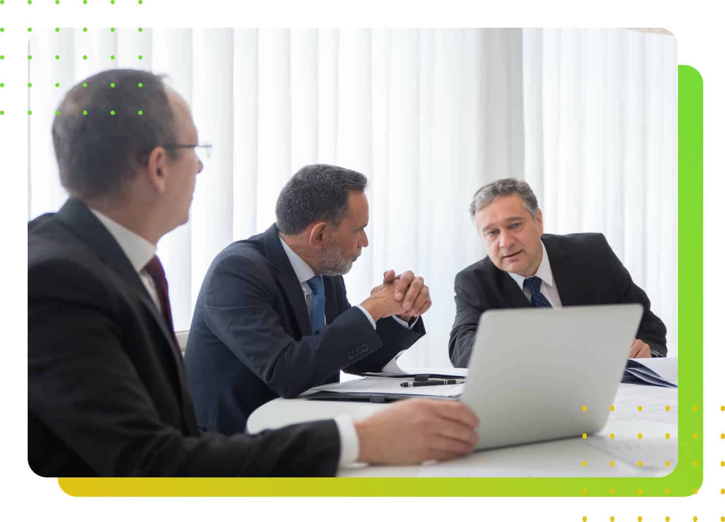 A man in suit with two others, staring at the laptop while talking