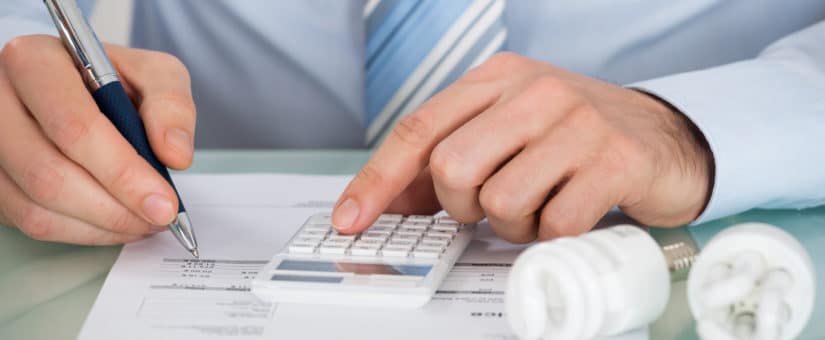 Close-up Of Businessman Using Calculator With Fluorescent Light Bulb At Desk